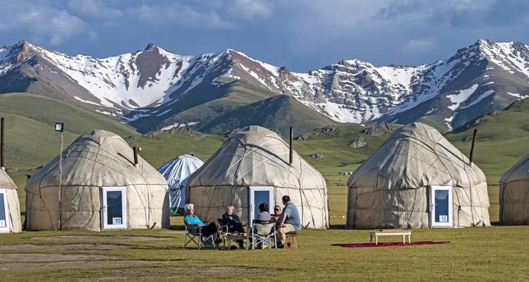 A group of people sitting outside yurts in the mountains.