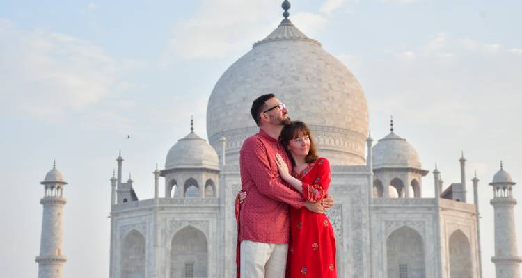 Couple in traditional attire embracing in front of the gleaming Taj Mahal under soft morning light.