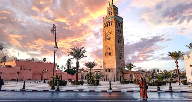 Hoge minaret voor een zonsonderganglucht met palmbomen.