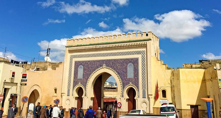 Een grote sierlijke stadspoort waar mensen doorheen lopen.