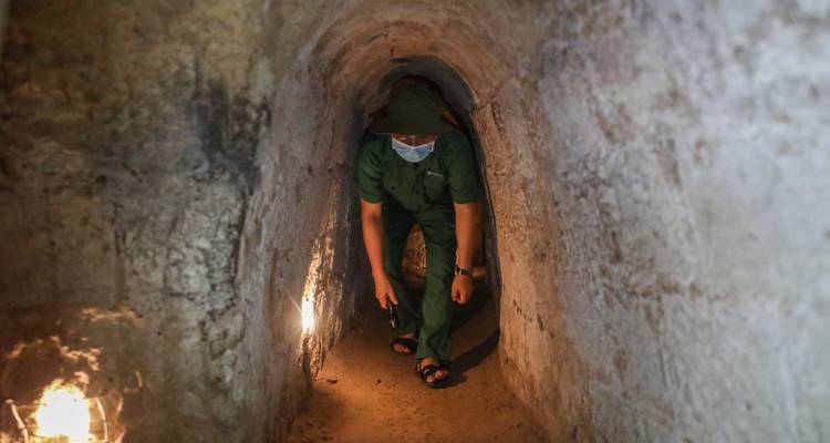 Persoon in een militair uniform die een smalle tunnel ondergronds verkent.