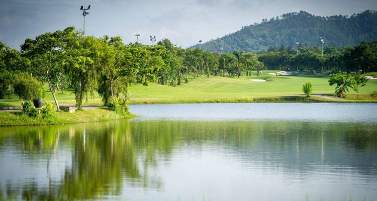 Golfbaan met een meer en heuvels in de verte.