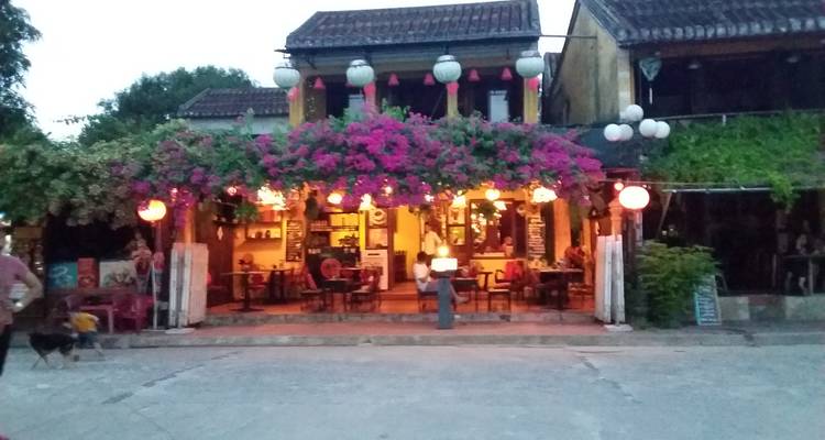 Straatzicht van een gezellig restaurant met kleurrijke bloemen en lantaarns.