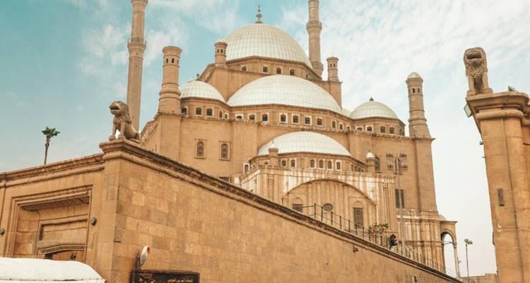Historische moskee met grote koepels en minaretten tegen een blauwe hemel.