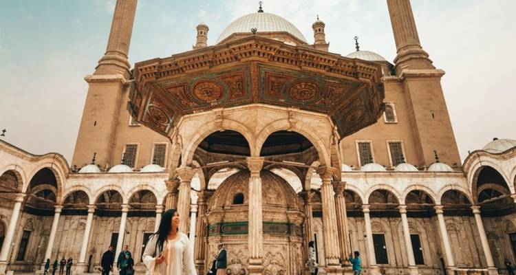 Historisch gebouw met bogen en koepels, met een persoon die op de voorgrond loopt.