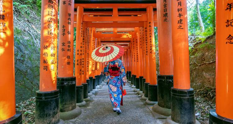 Mujer en kimono caminando por un corredor de puertas torii rojas.