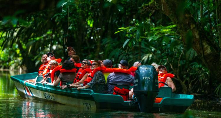Gruppe von Menschen in einem Boot mit Schwimmwesten, die durch eine üppige Dschungel-Wasserstraße navigieren.
