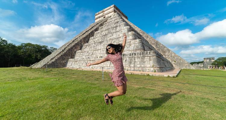 Une personne qui saute devant une structure pyramidale célèbre dans un champ herbeux.
