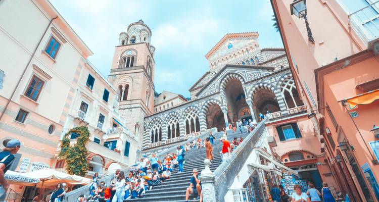 Des foules sur le grand escalier menant à la cathédrale d'Amalfi avec sa façade rayée saisissante et son clocher.