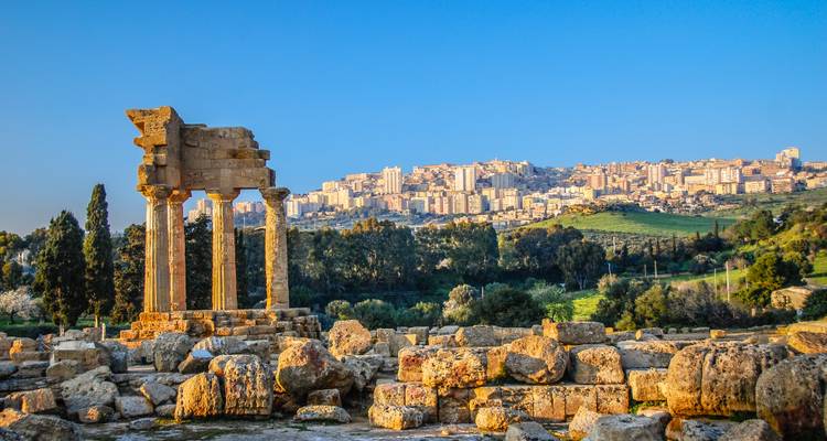 Ruines d'un ancien temple de pierre se dressant contre un village perché sur une colline lointaine baigné dans la douce lumière du soir.