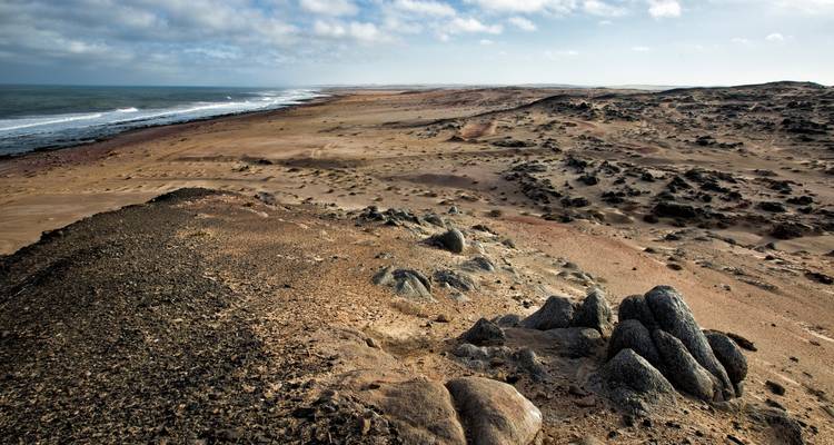 Weite Wüstenküste mit Felsen und Ozean.