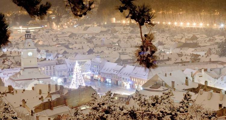 Luchtfoto van een met sneeuw bedekte stad met lichtjes en een feestelijke sfeer.