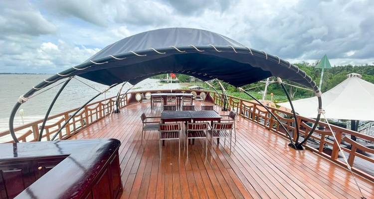Pont de bateau vide avec tables et chaises sous un auvent par temps nuageux.