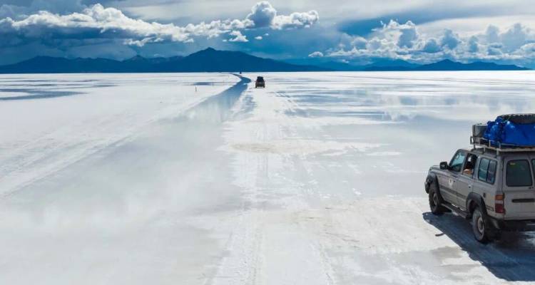4x4 vehicles driving across endless white expanse of Uyuni salt flats under dramatic clouds