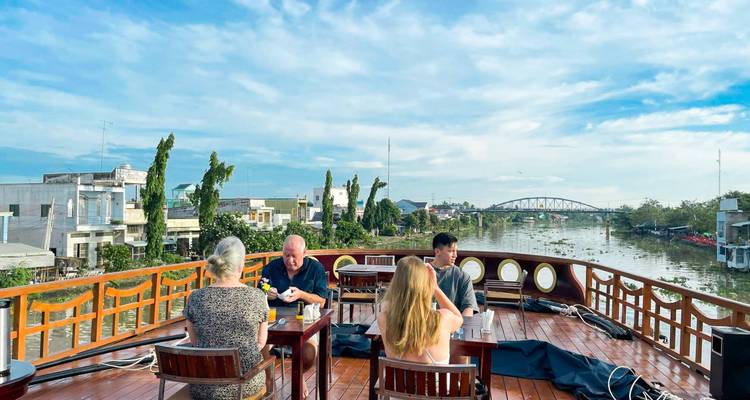 Personas cenando en una terraza abierta con vista al río.