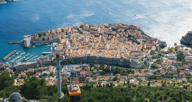 Le téléphérique descend vers la ville fortifiée de Dubrovnik et le port en contrebas d'une mer baignée de soleil.