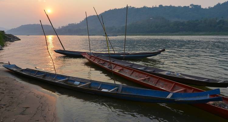 Lange Boote auf einem Fluss bei Sonnenuntergang mit Hügeln im Hintergrund.