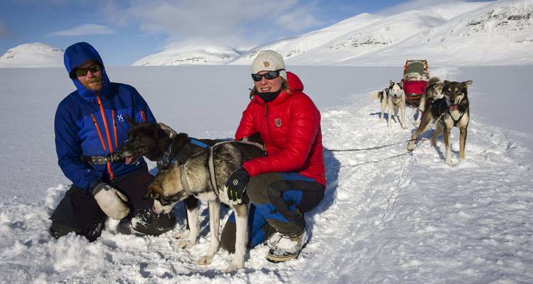 Two people petting huskies in the snow.