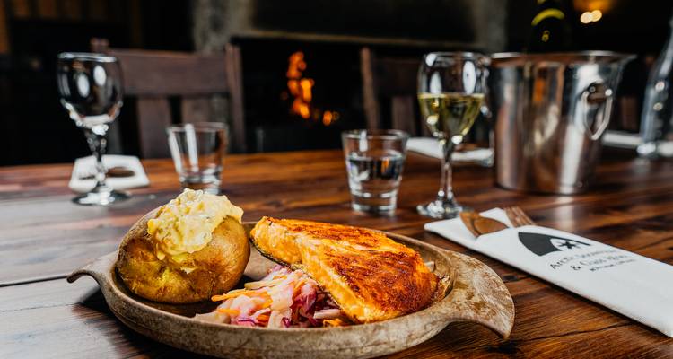 Un couvert en bois avec un repas comprenant une pomme de terre au four and du saumon.