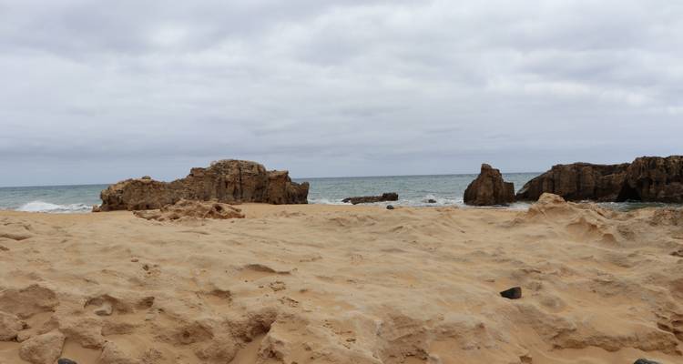 Plage de sable avec formations rocheuses et ciel nuageux.