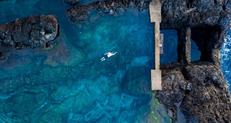 Personne nageant dans un bassin naturel de roche dans une eau bleue claire.