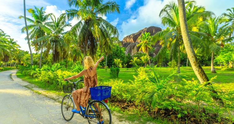 Person cycling on a tropical path surrounded by greenery.