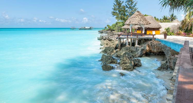 Ein atemberaubender Küstenblick mit einer Hütte, die über Felsen hängt, und leuchtend türkisfarbenem Wasser.