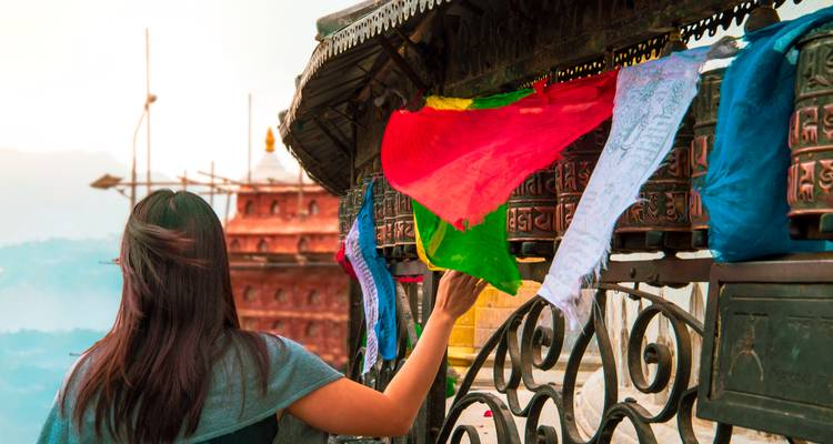 Eine Person, die Gebetsmühlen berührt, mit Flaggen im Hintergrund