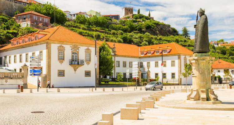 Statue vor Gebäuden im Kolonialstil mit orangen Dächern.