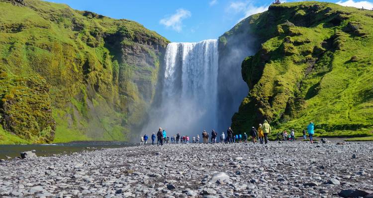 Touristen stehen am Fuß des Skogafoss-Wasserfalls.