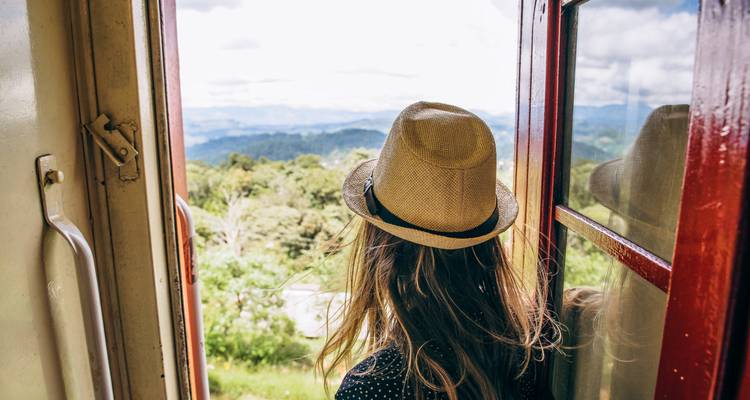 Person, die aus einer Zugtür auf eine malerische Landschaft blickt.