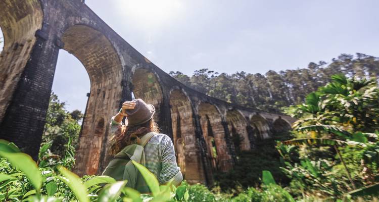 Reiziger die staat bij een groot stenen viaduct in een bosrijk gebied.