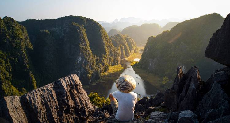 Person, die auf Klippen sitzt und auf ein Tal blickt.