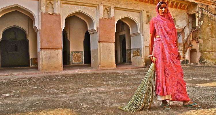 Femme en tenue traditionnelle debout devant un bâtiment historique.