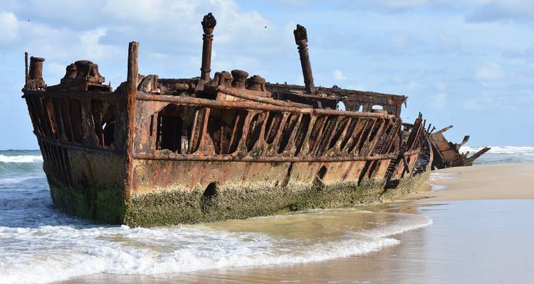 Une épave rouillée partiellement ensevelie dans le sable sur une plage.