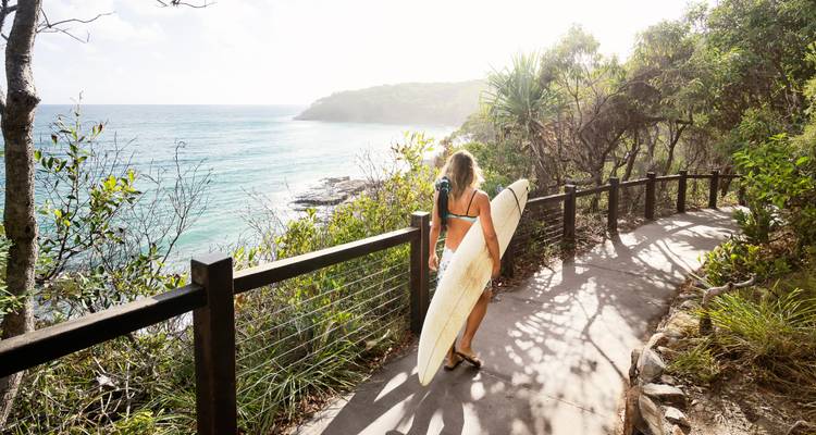 Personne marchant avec une planche de surf le long d'un sentier côtier.