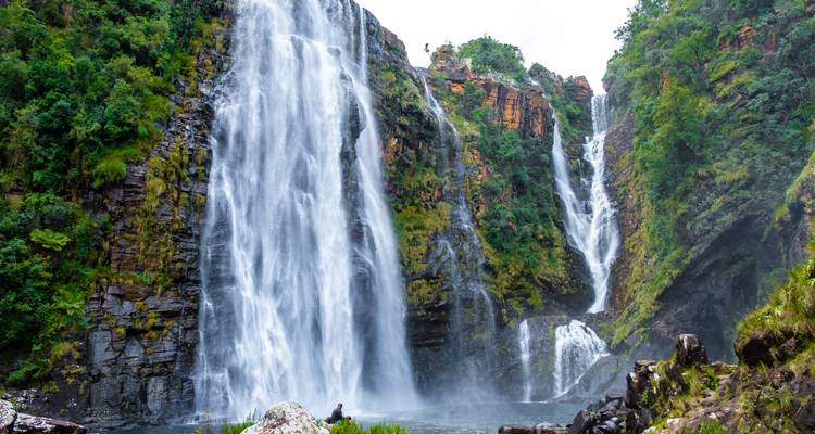 Wasserfall in üppigem Wald mit Person, die die Aussicht bewundert.