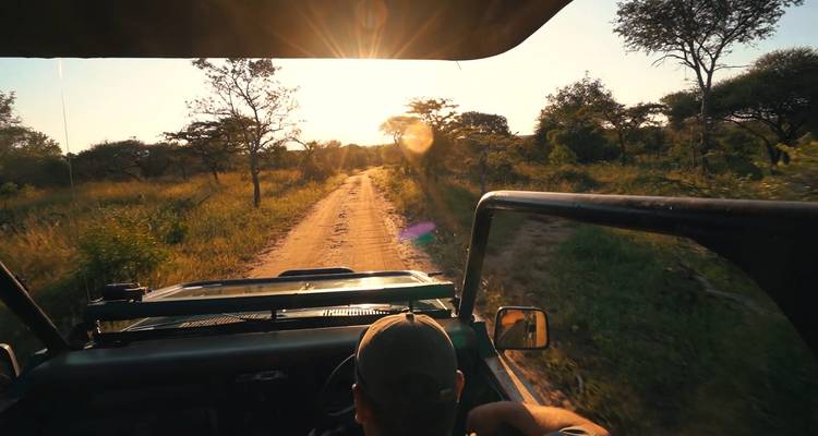 Ein Safari-Fahrzeug, das bei Sonnenuntergang auf einer staubigen Straße fährt.