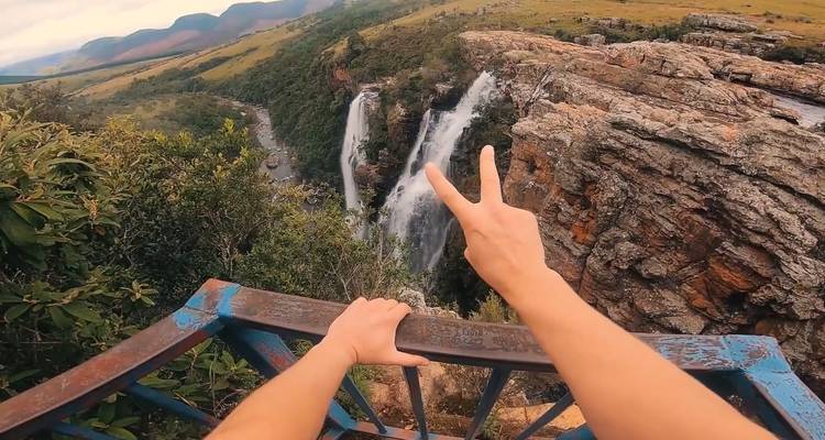 Eine Person, die sich über ein Geländer lehnt, um einen Wasserfall zu fotografieren.