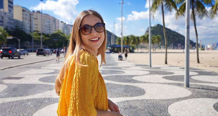 Frau lächelnd auf einer Strandpromenade mit ikonischem wellengemustertem Pflaster.
