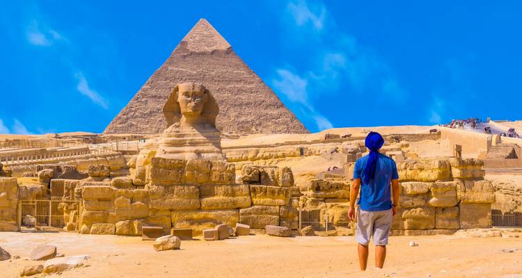Person standing in front of the Great Pyramid and the Sphinx.
