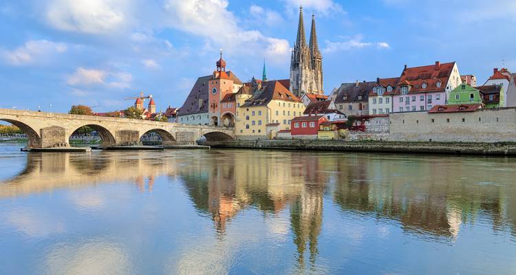 Colorful medieval old town of Regensburg with stone bridge and cathedral reflected in the Danube River on a bright day.