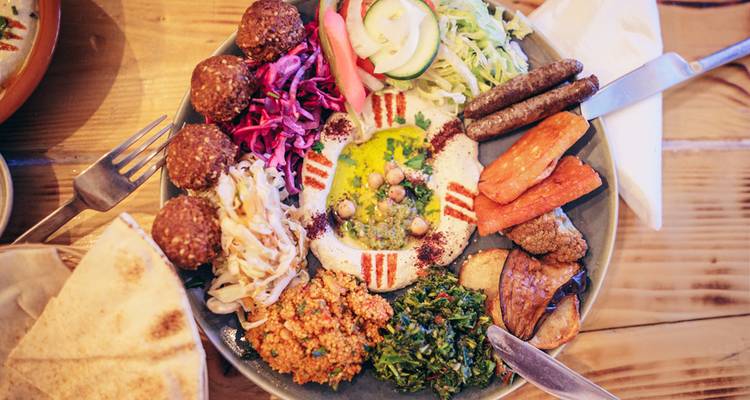 Colorful Mediterranean mezze plate with falafel, hummus and fresh vegetables on wooden table.