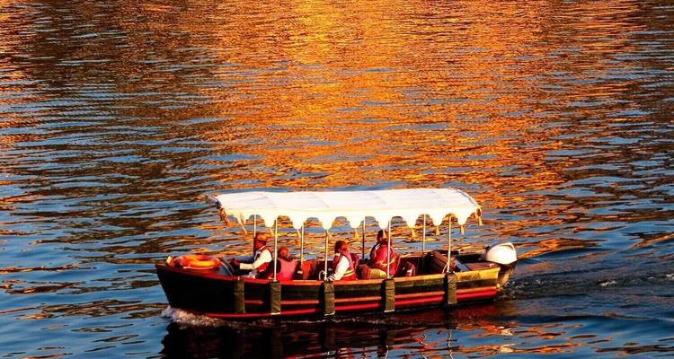 Boat with people navigating on a shimmering lake during sunset.