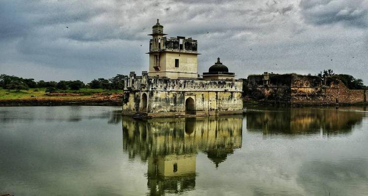 Dilapidated structure in a lake with cloudy skies reflecting on water.
