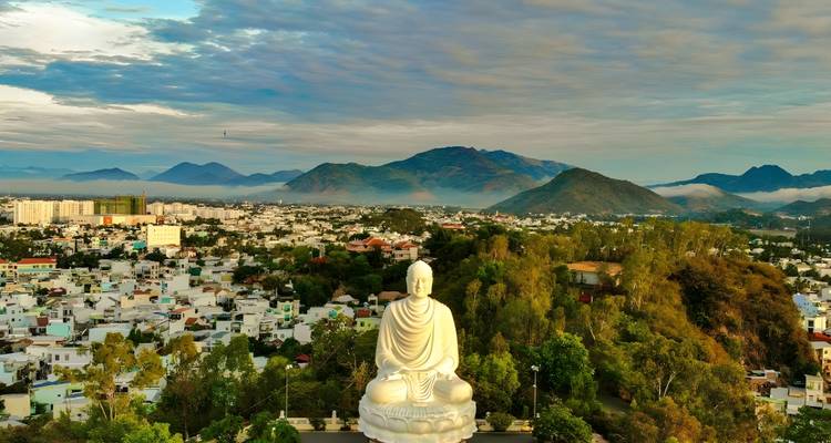 Statue géante de Bouddha surplombant une ville avec des montagnes.