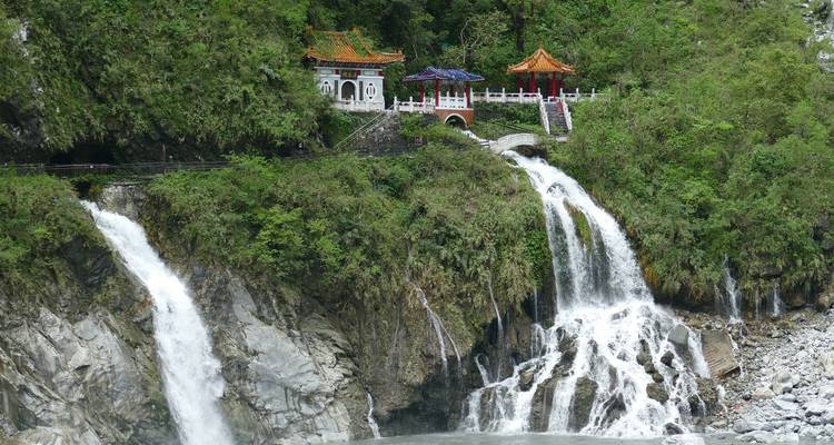 Ein malerischer Wasserfall mit traditioneller Architektur in üppigem Grün.