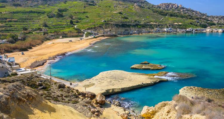 Baie turquoise avec des collines verdoyantes en terrasses et des affleurements rocheux sur la côte de l'île maltaise.