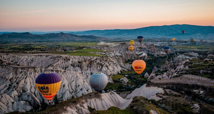Hot air balloons flying over a rocky landscape during sunrise.