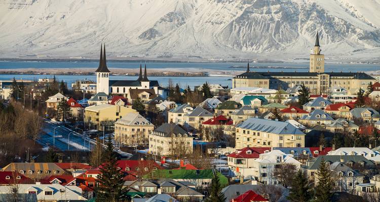 Winterliches Stadtbild von Reykjavik mit farbenfrohen Dächern und schneebedeckten Bergen im Hintergrund.